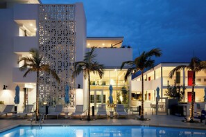 Un hotel modern amb piscina, gandules i palmeres.