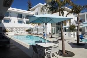 A poolside area with a pool, lounge chairs, umbrellas, and a white building with balconies. - Courtyard by Marriott Santa Barbara Downtown (Santa Barbara)
