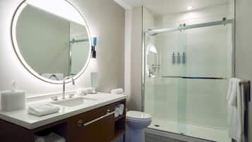A modern bathroom with a large mirror, a sink, a toilet, and a glass-enclosed shower.