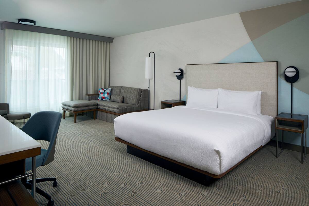 Quarto de hotel com uma cama grande, uma escrivaninha, uma cadeira, um sofá e um abajur.