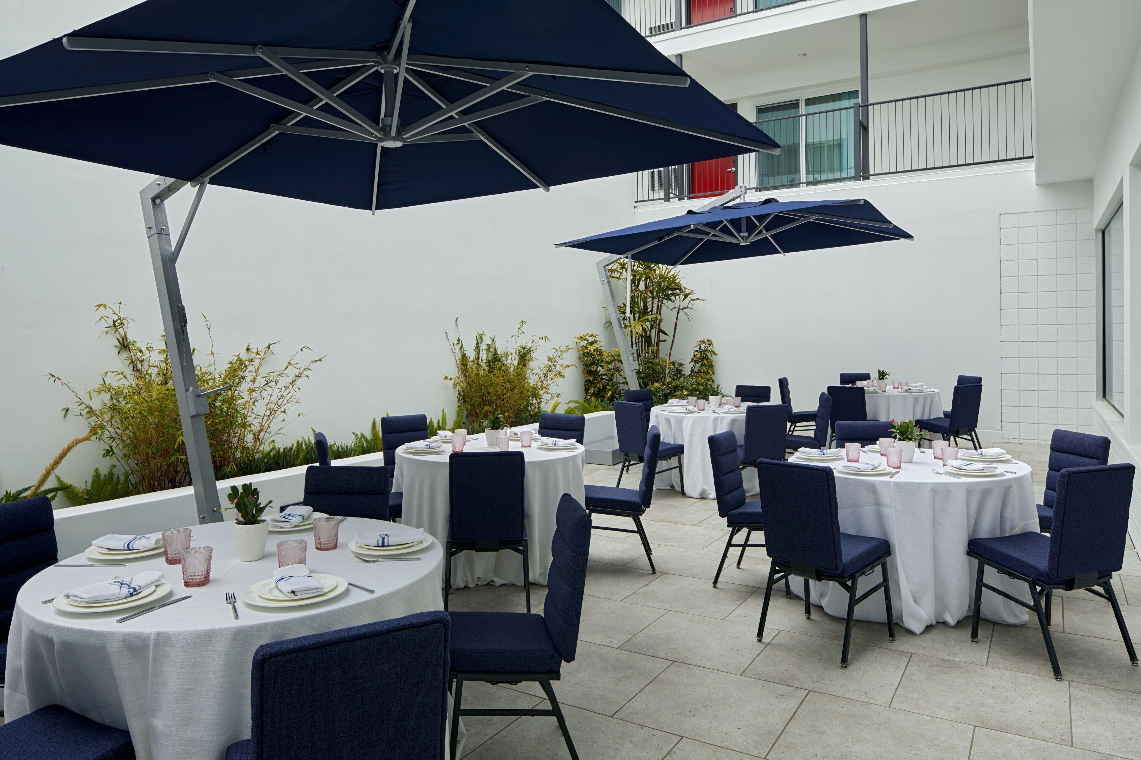 A rooftop dining area with round tables, blue chairs, and umbrellas.