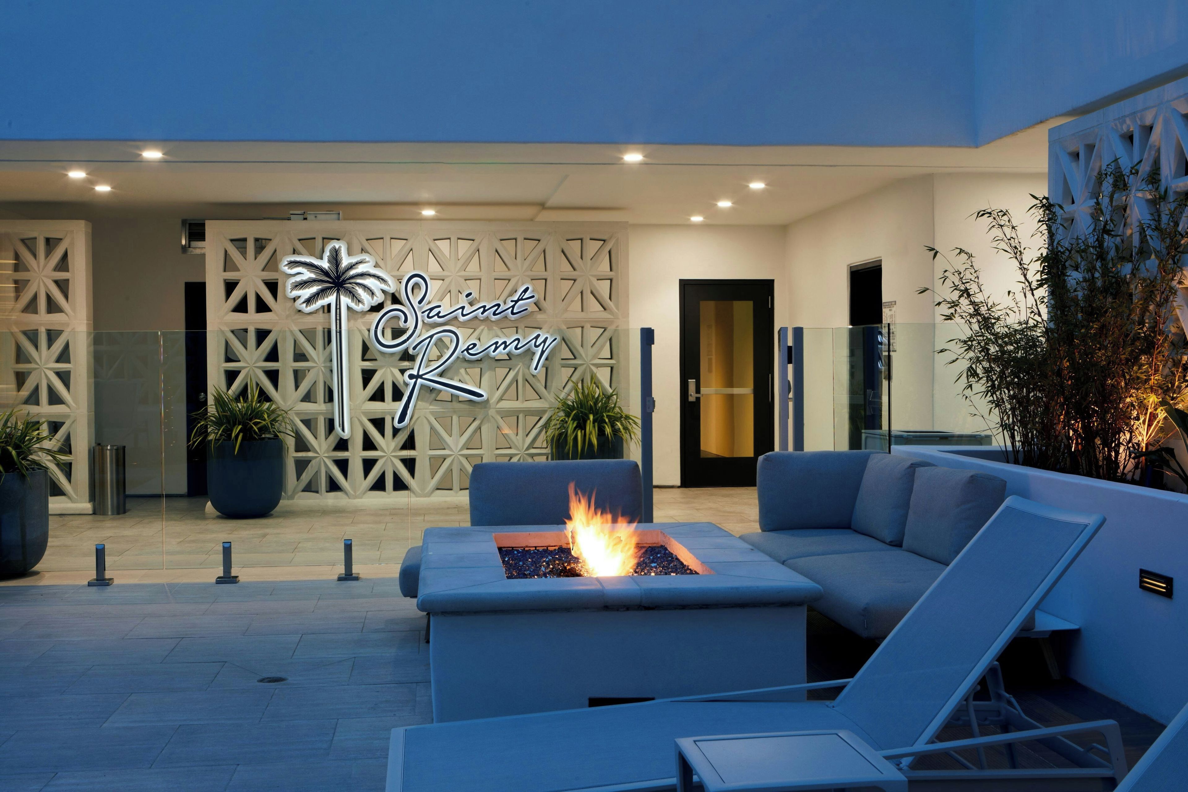 An outdoor seating area with a fire feature, a decorative wall with a palm tree sign, and potted plants.