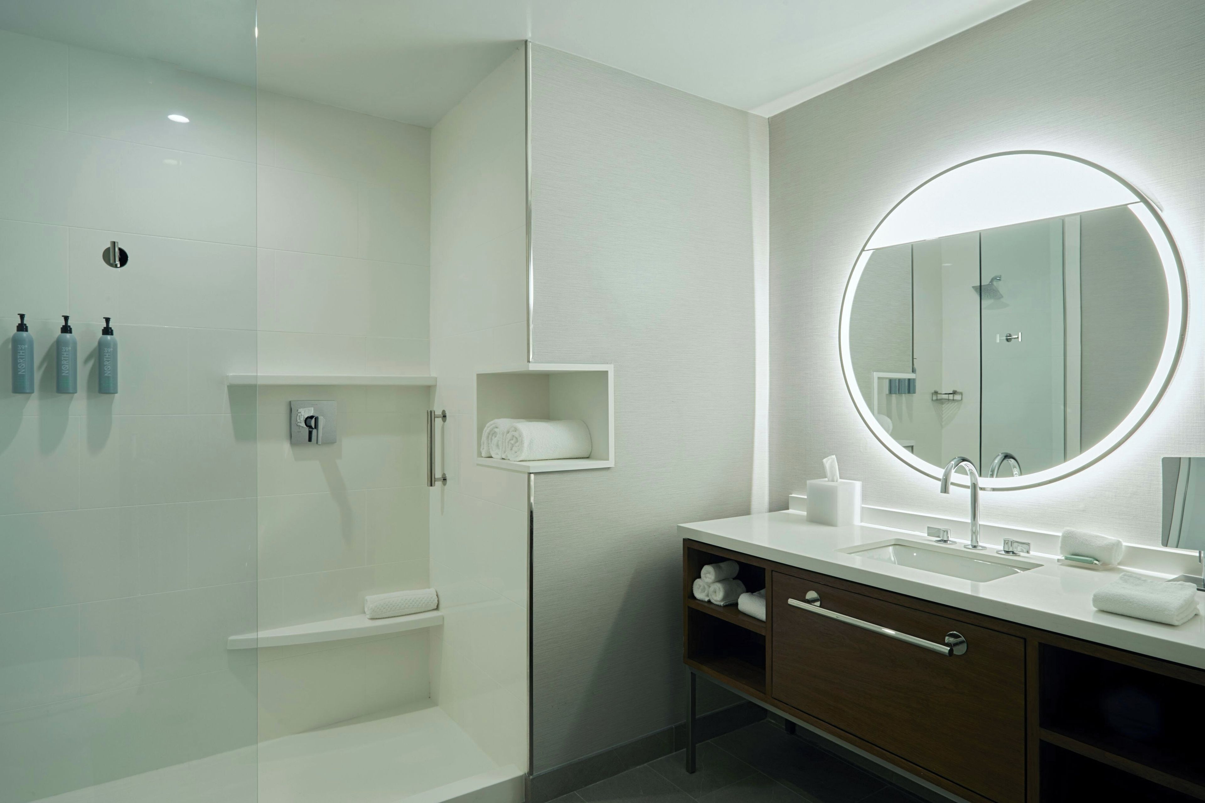 A modern bathroom with a glass-enclosed shower, a vanity with a mirror, and toiletries on the wall.