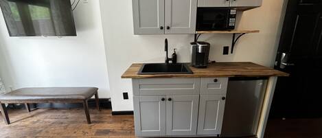 A compact kitchen with grey cabinets, a wooden countertop, a black microwave, and a built-in dishwasher.