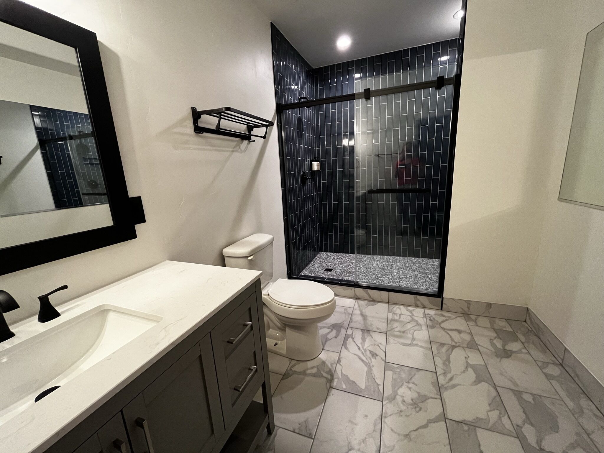 A bathroom with a white sink, dark cabinets, a toilet, and a glass-enclosed shower with dark tiles.