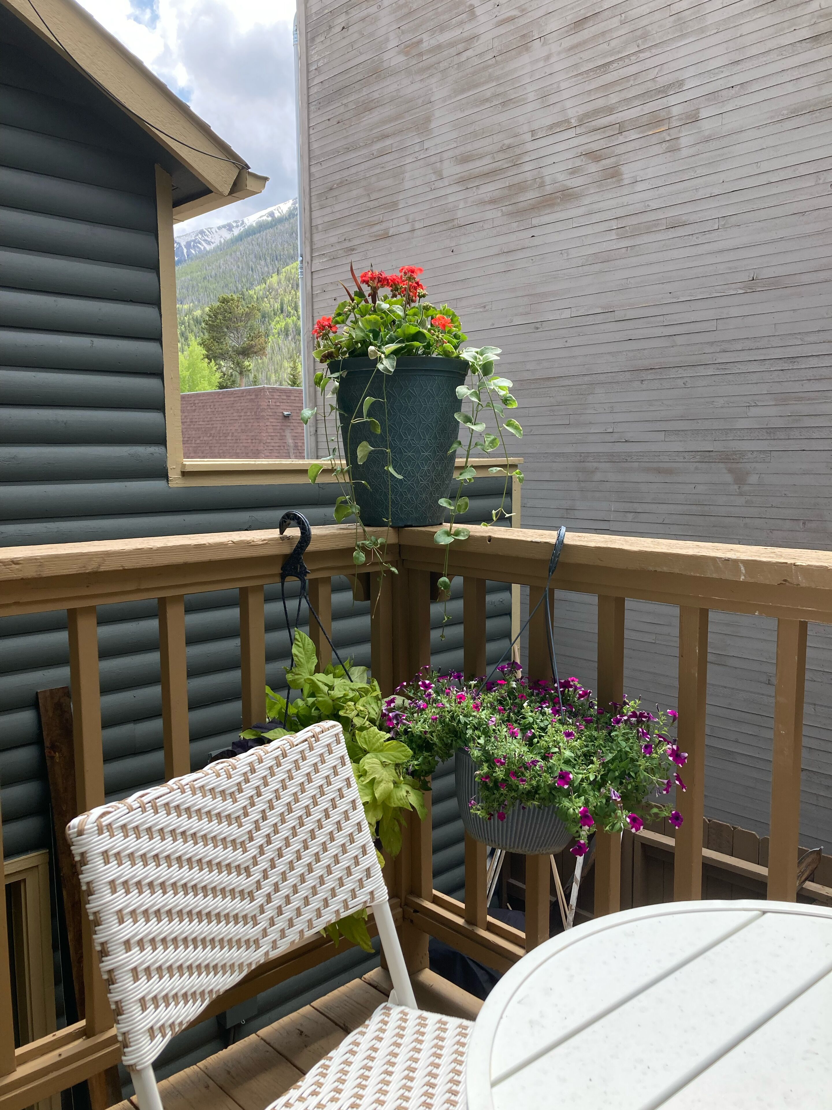 En træterrasse med en fletstol og et bord, omgivet af plantekrukker.