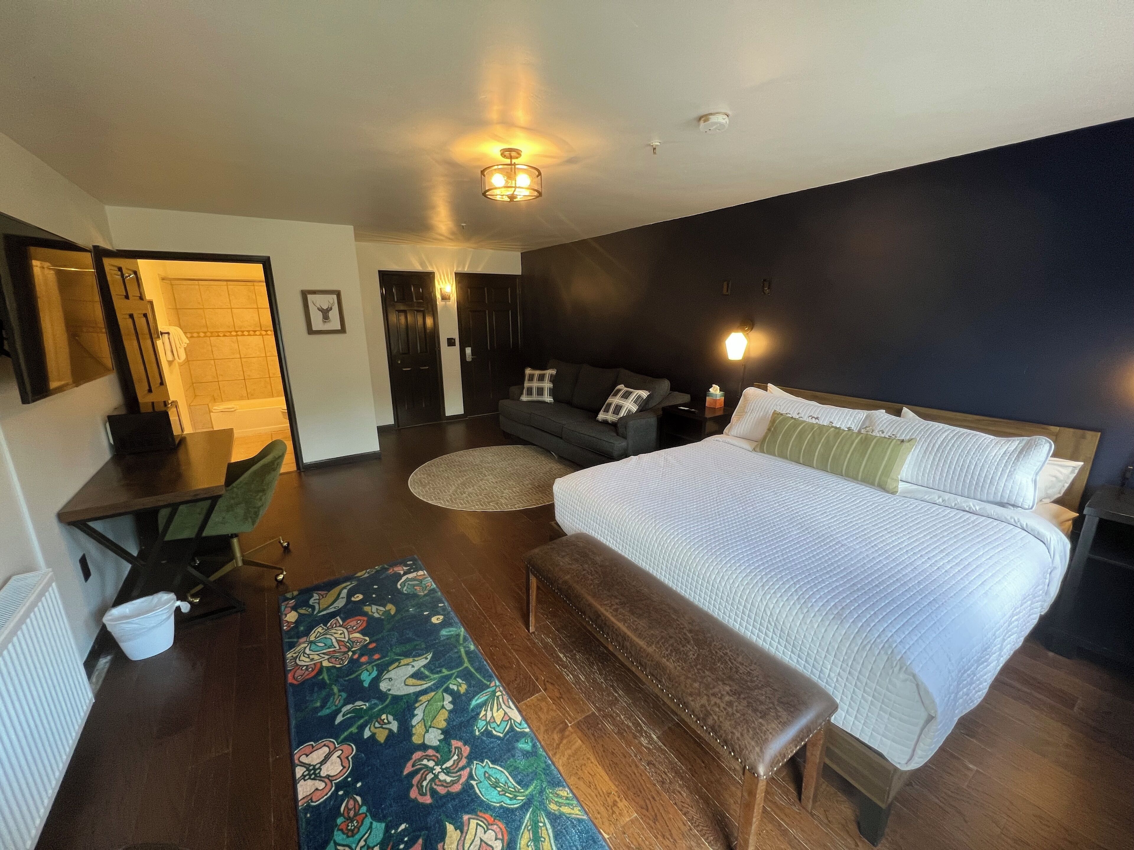 Een moderne hotelkamer met een groot bed, een bankje, een sofa, een bureau en een zichtbare badkamer door een open deur.