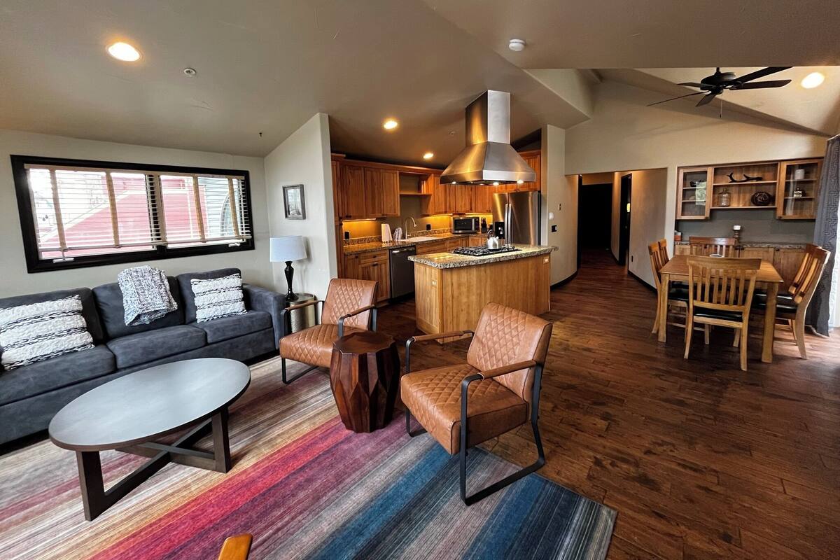 A spacious living area with a sofa, coffee table, and chairs, a kitchen with wooden cabinets, and a dining area with a table and chairs.