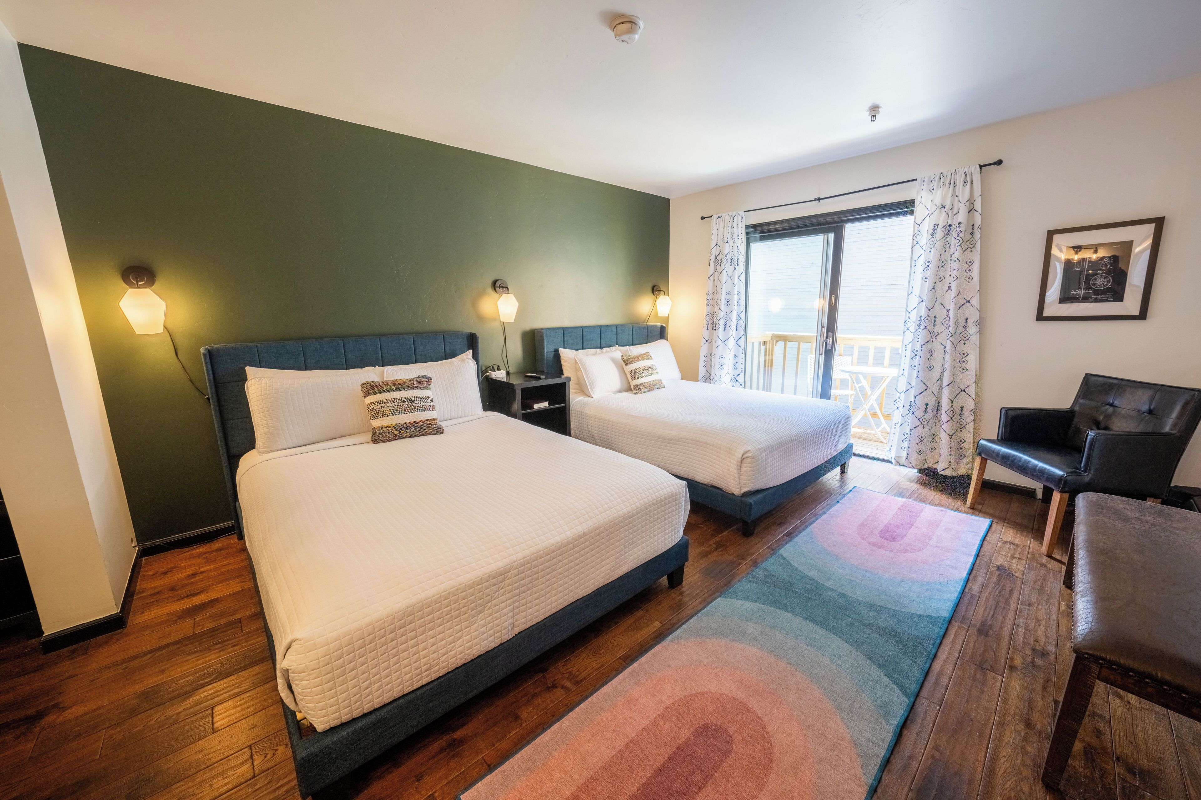 A hotel room with two beds, a desk, and a balcony.