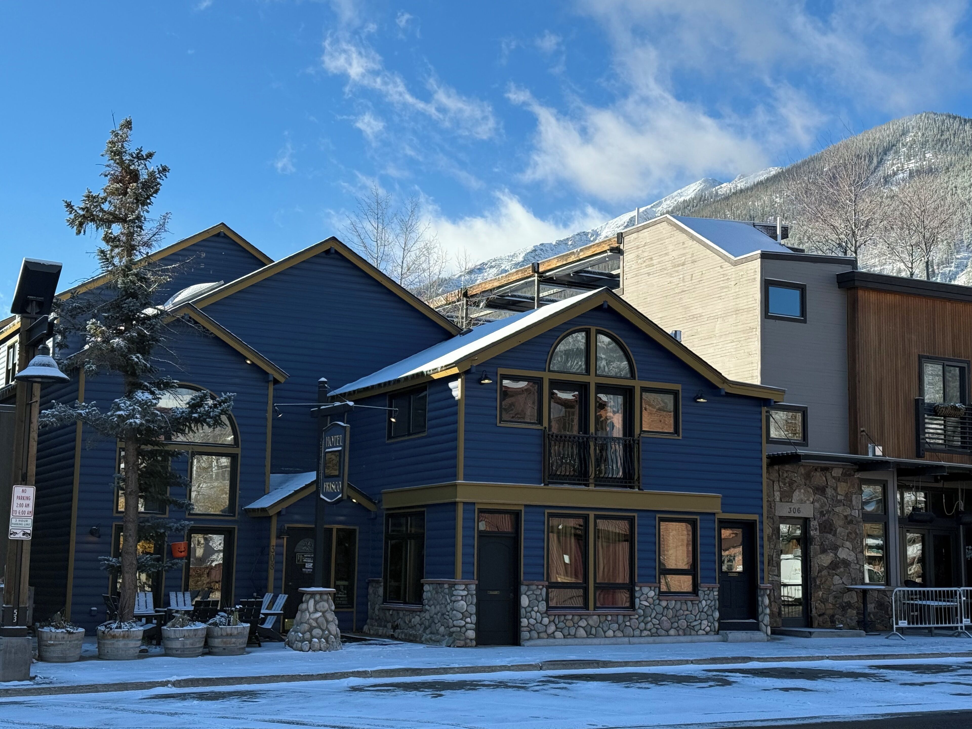 Et hotel med blå facade, stenelementer og et bjerglandskab i baggrunden.