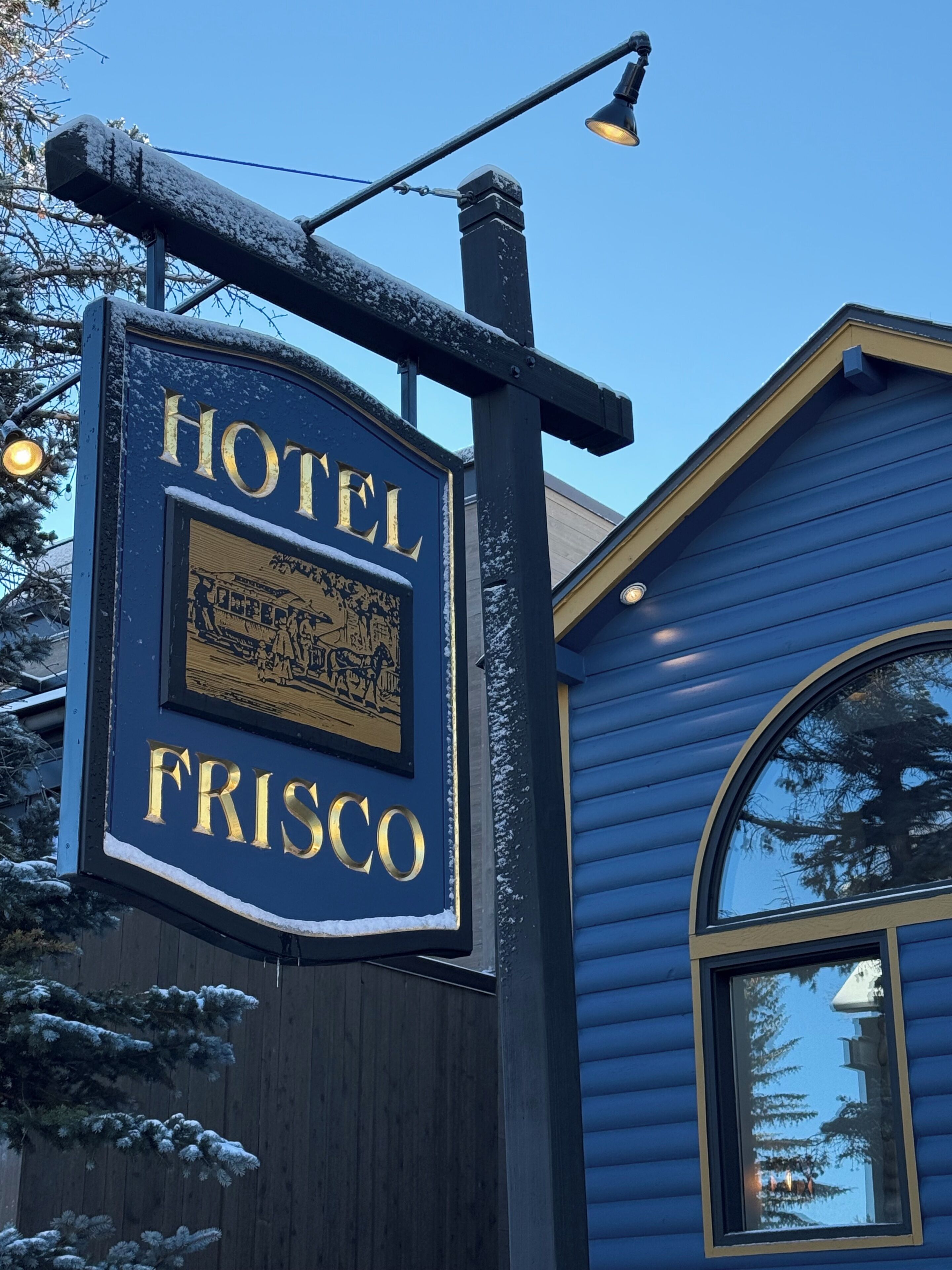Une enseigne d’hôtel portant l’inscription « HÔTEL FRISCO » et un bâtiment à la façade bleue.