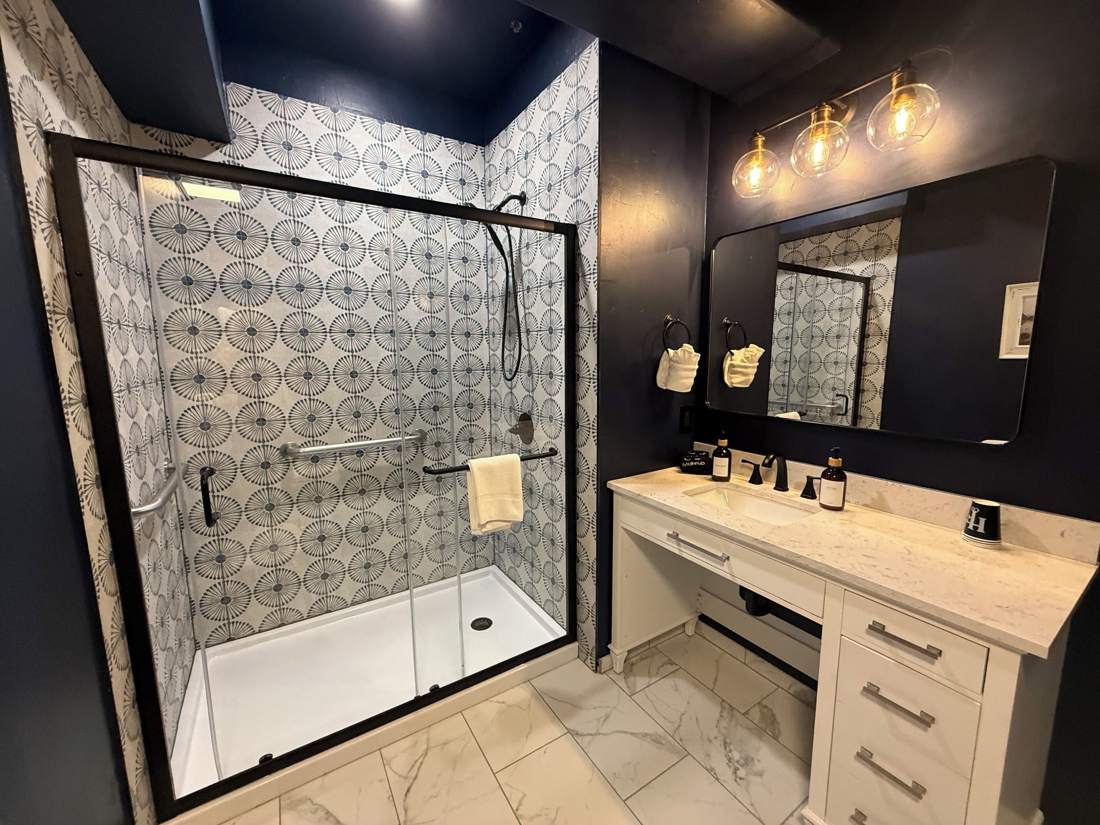 A modern bathroom with a glass-enclosed shower, a vanity with a mirror, and a marble floor.