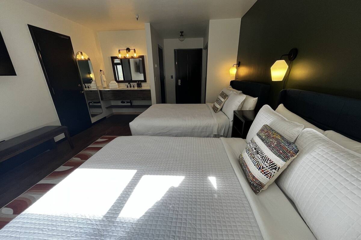 A hotel room with two beds, a large mirror, a vanity with a mirror, and a nightstand with a lamp.