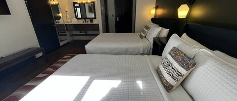 Une chambre d’hôtel avec deux lits, un grand miroir, une coiffeuse avec un miroir et une table de chevet avec une lampe.