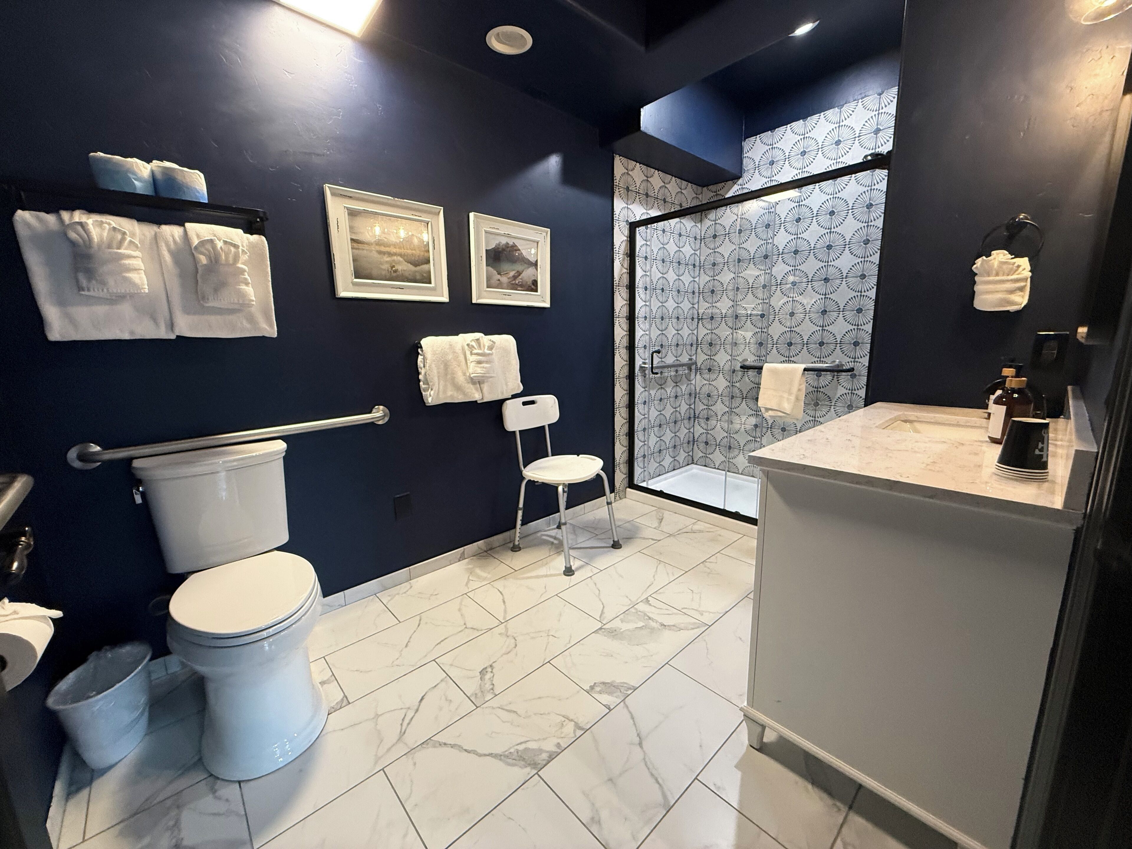 Un baño moderno con una pared azul oscuro, un inodoro blanco, un bidé, una ducha con puerta de vidrio con diseño y un suelo de baldosas de mármol.