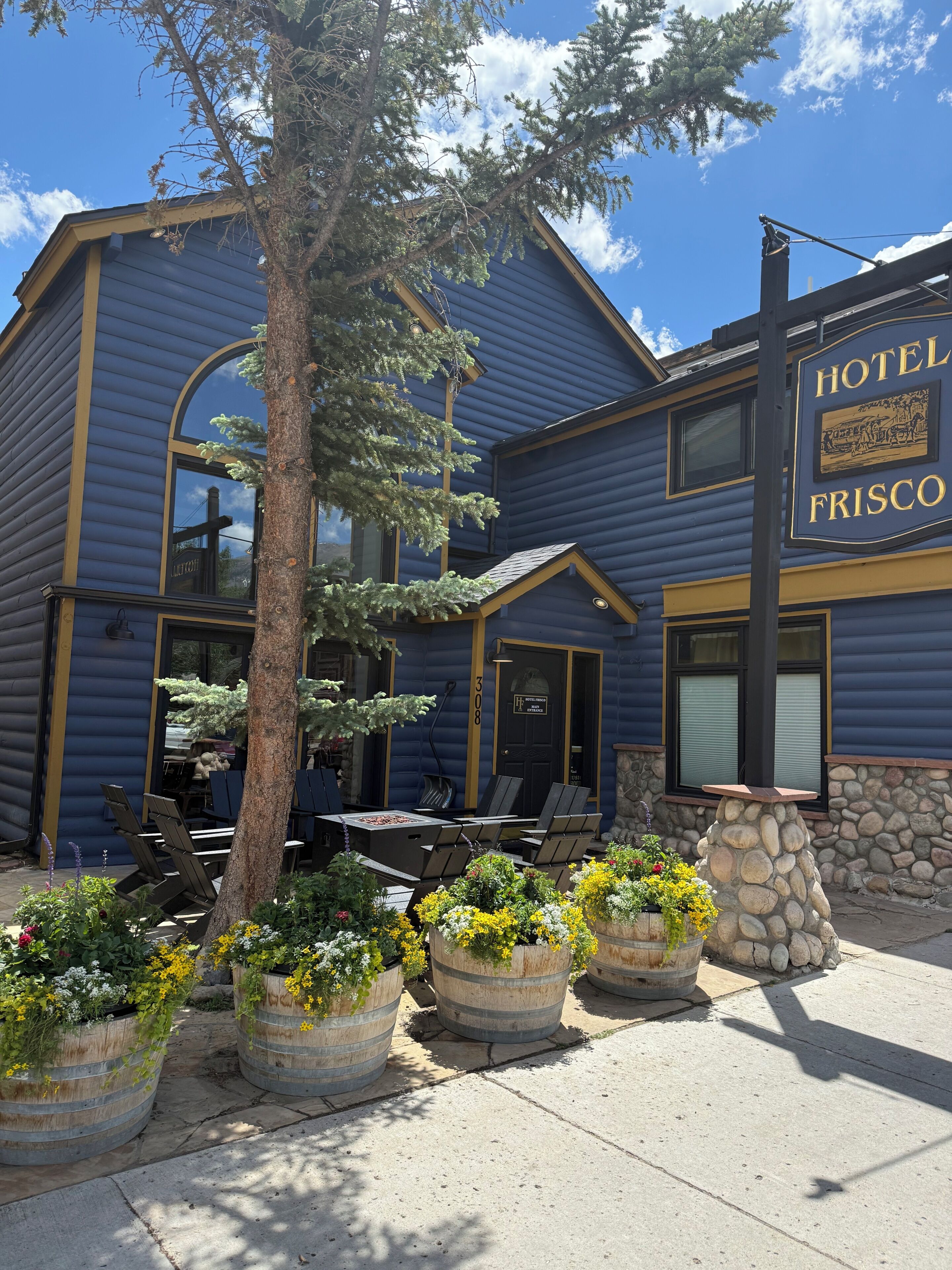 Un hotel con fachada azul, zona de estar al aire libre y un pilar de piedra.