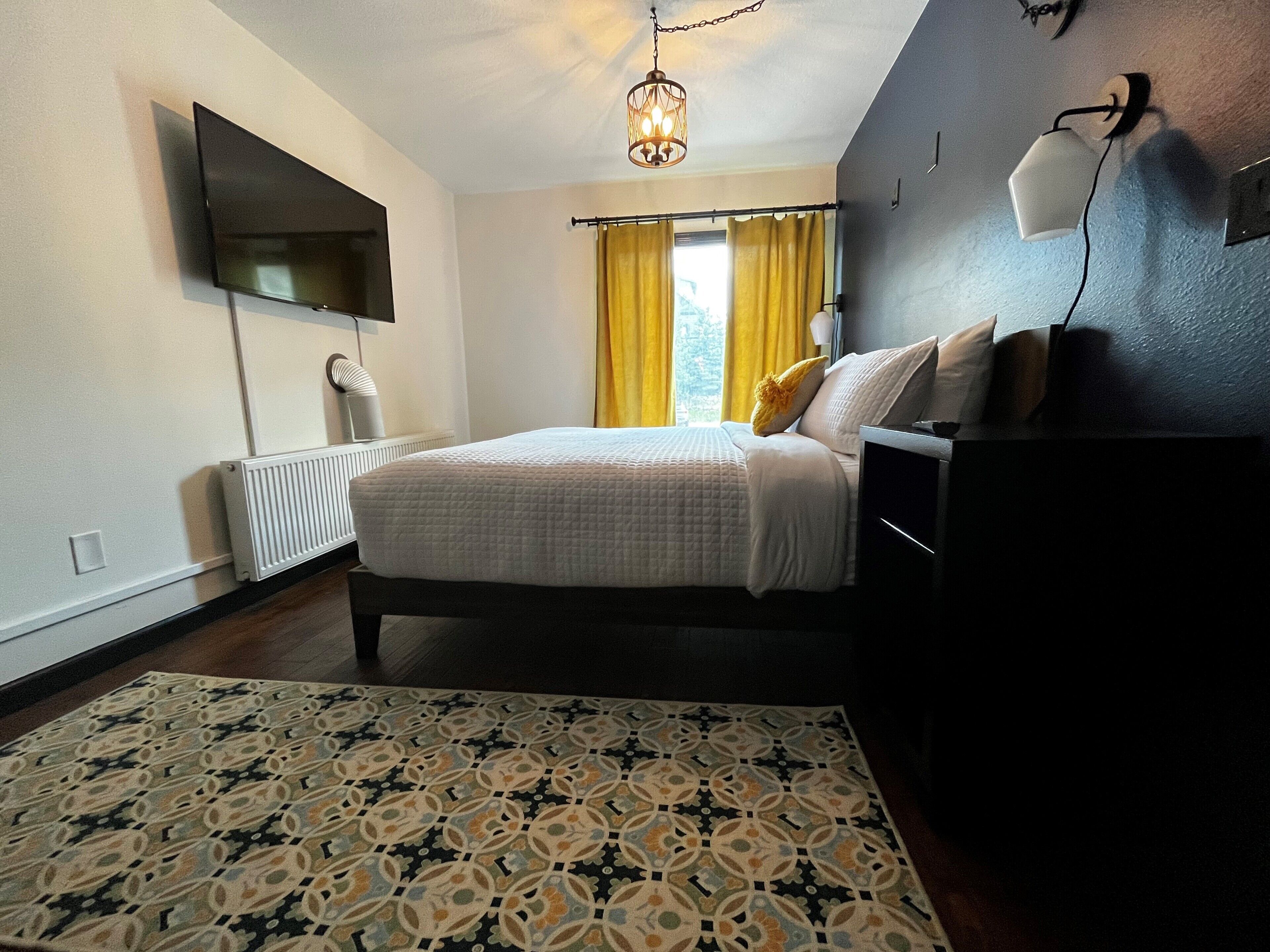 Una camera da letto moderna con un letto grande, una TV a schermo piatto montata a parete, un comodino e un tappeto decorato.