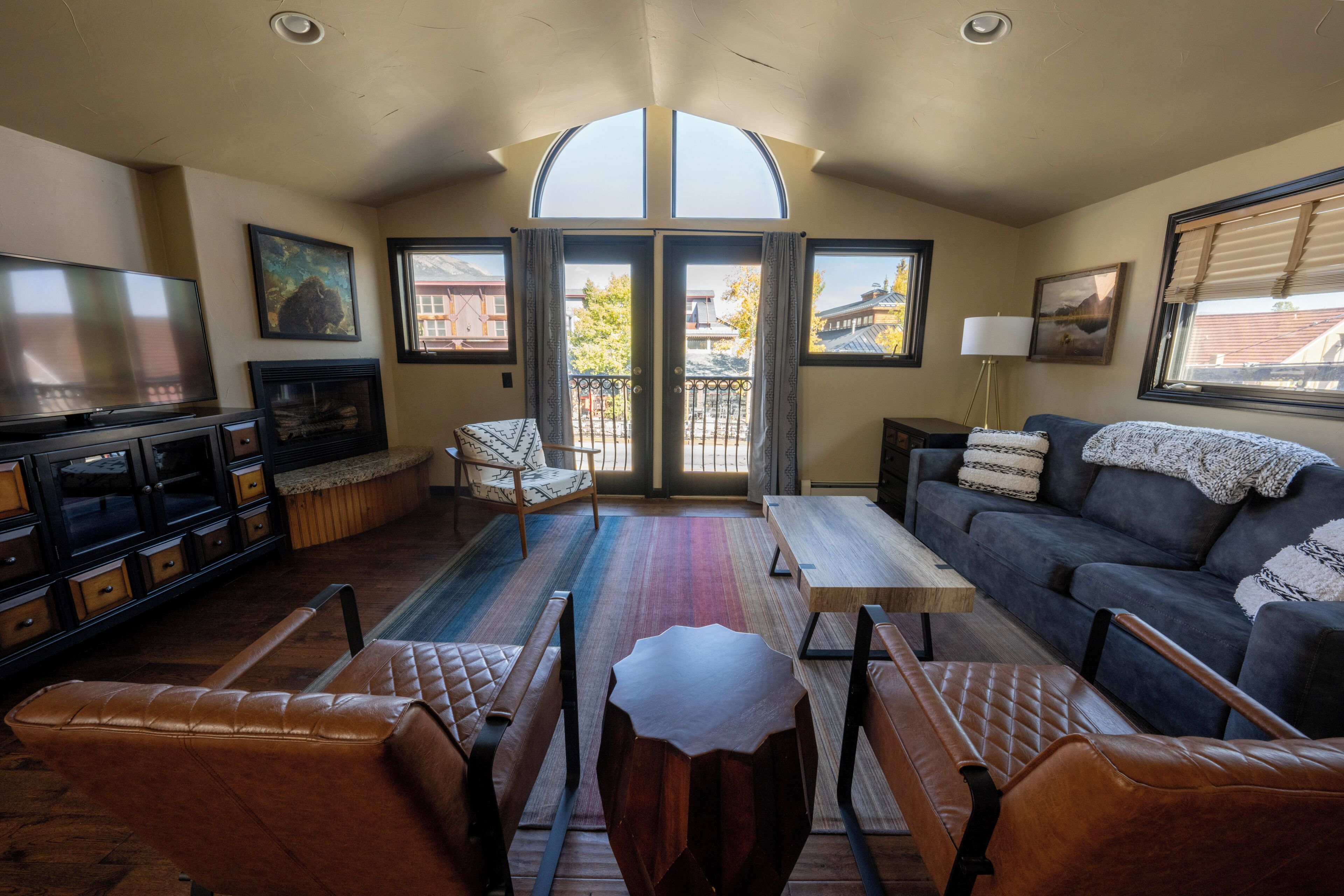 A living room with a television, sofa, chairs, a coffee table, and a view through the glass doors.