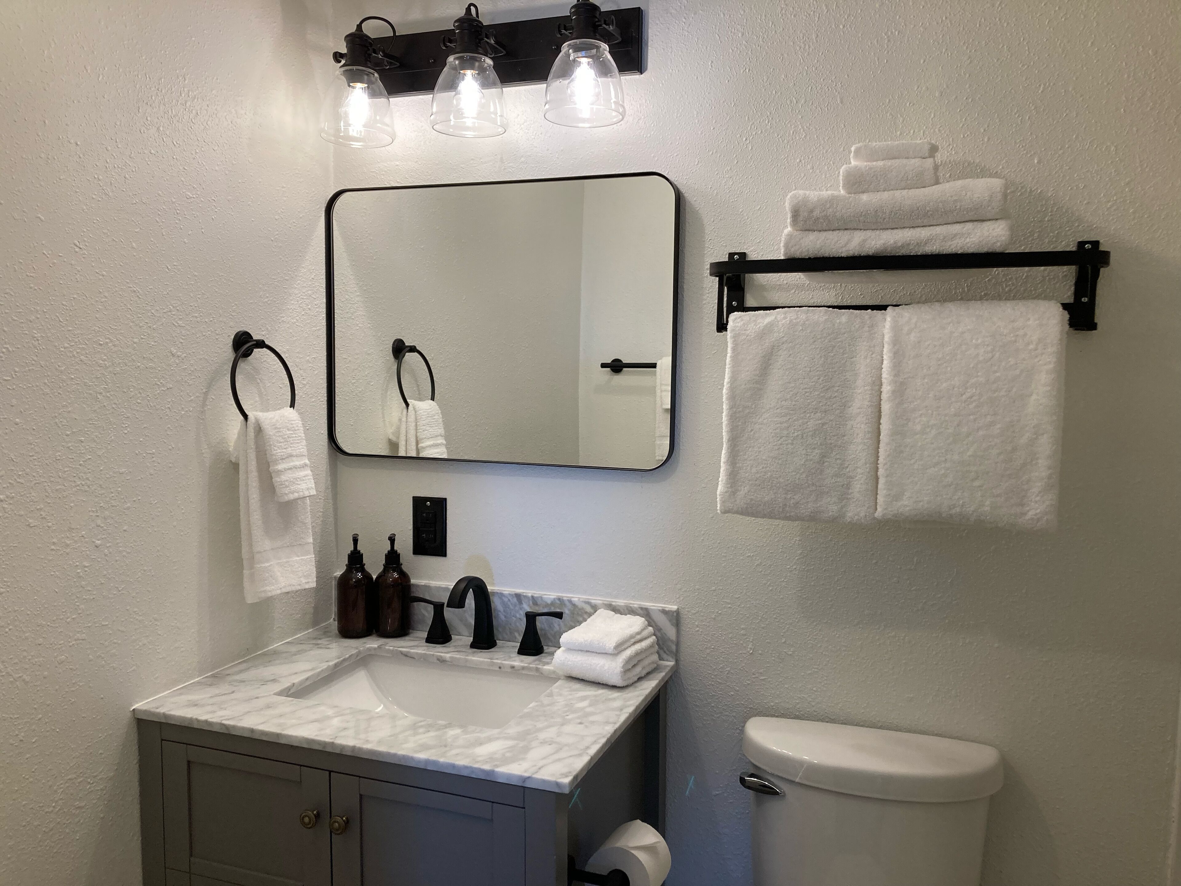 Ein Badezimmer mit einem weißen Waschbecken, einem Spiegel, einer Toilette und einem Handtuchhalter mit gefalteten Handtüchern.