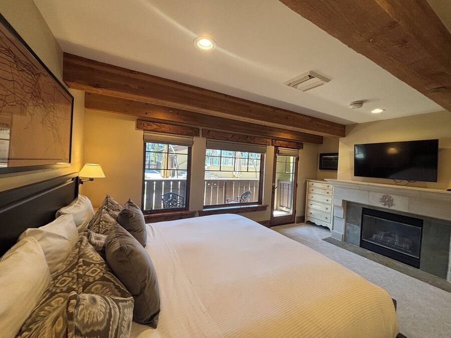 A bedroom with a large bed, a TV, a fireplace, and a balcony with windows.