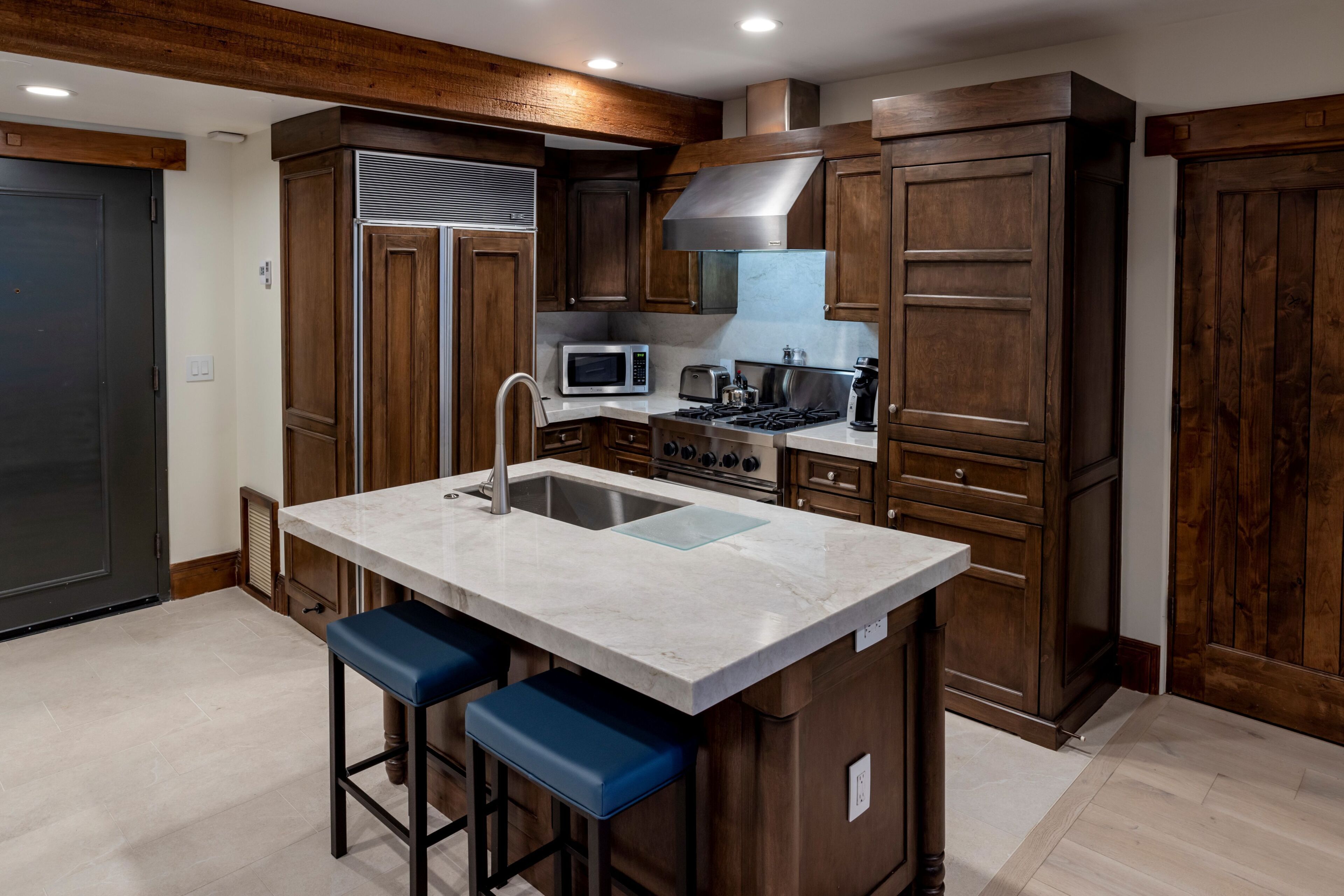 A kitchen with a central island, bar stools, a microwave, stove, and wooden cabinets.