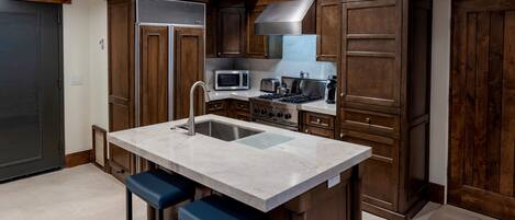 A kitchen with a central island, bar stools, a microwave, stove, and wooden cabinets.