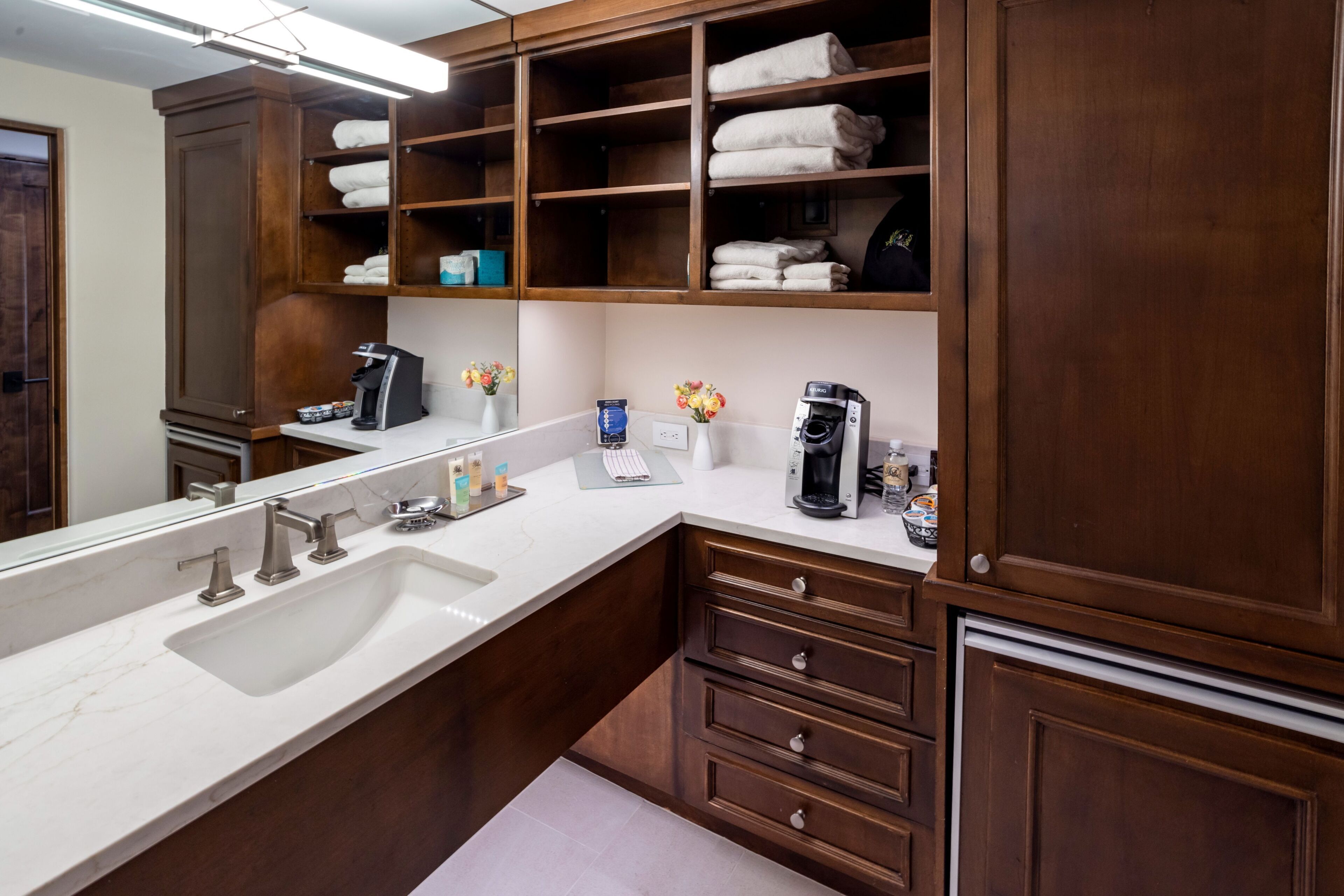 A bathroom with a large sink, wooden cabinets, and shelves with towels.