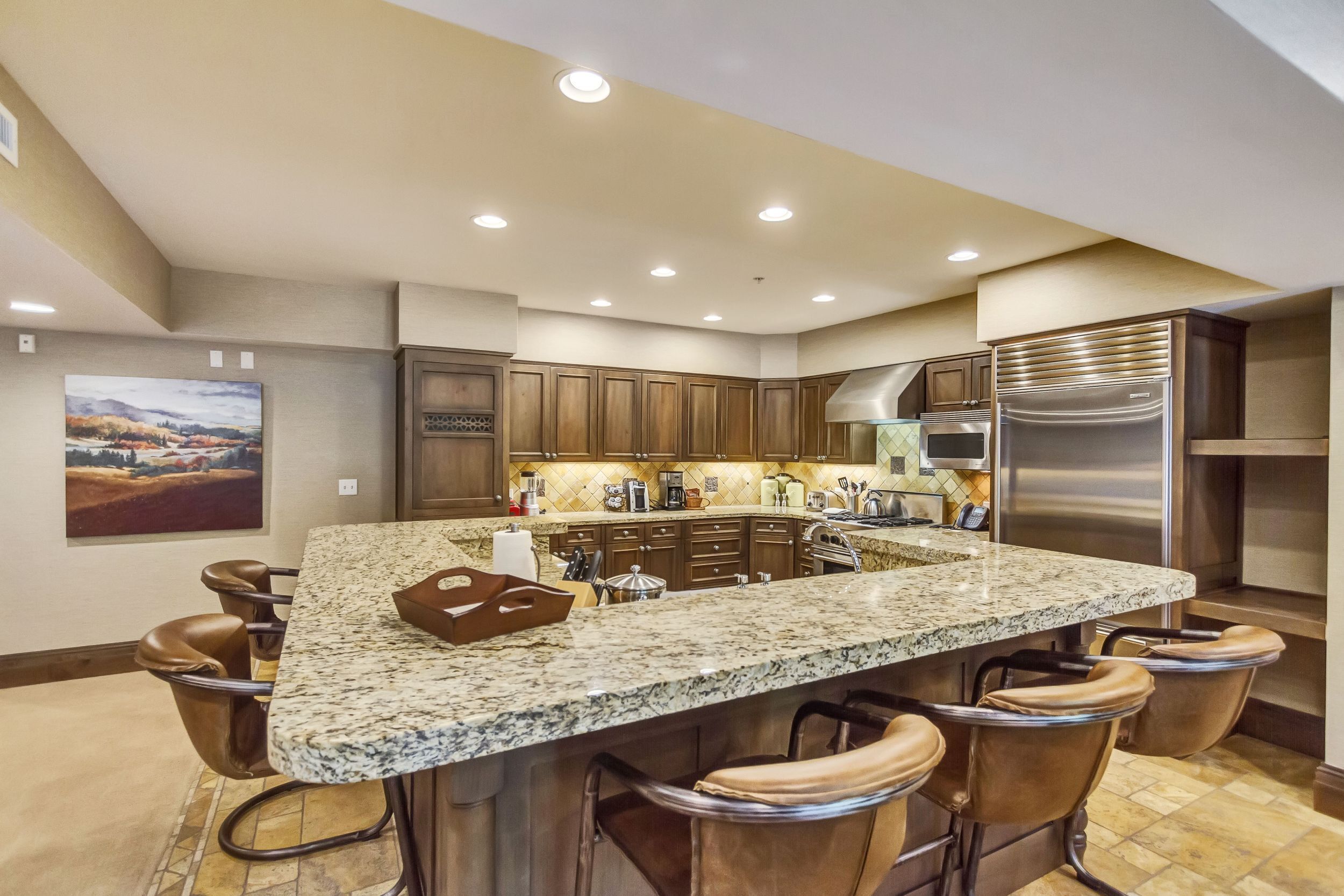 A kitchen with a large island, bar stools, wooden cabinets, and stainless steel appliances.