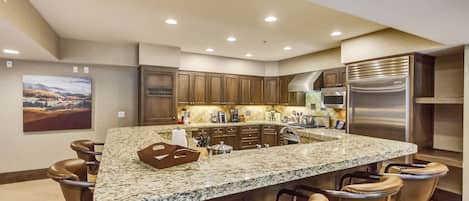 A kitchen with a large island, bar stools, wooden cabinets, and stainless steel appliances.