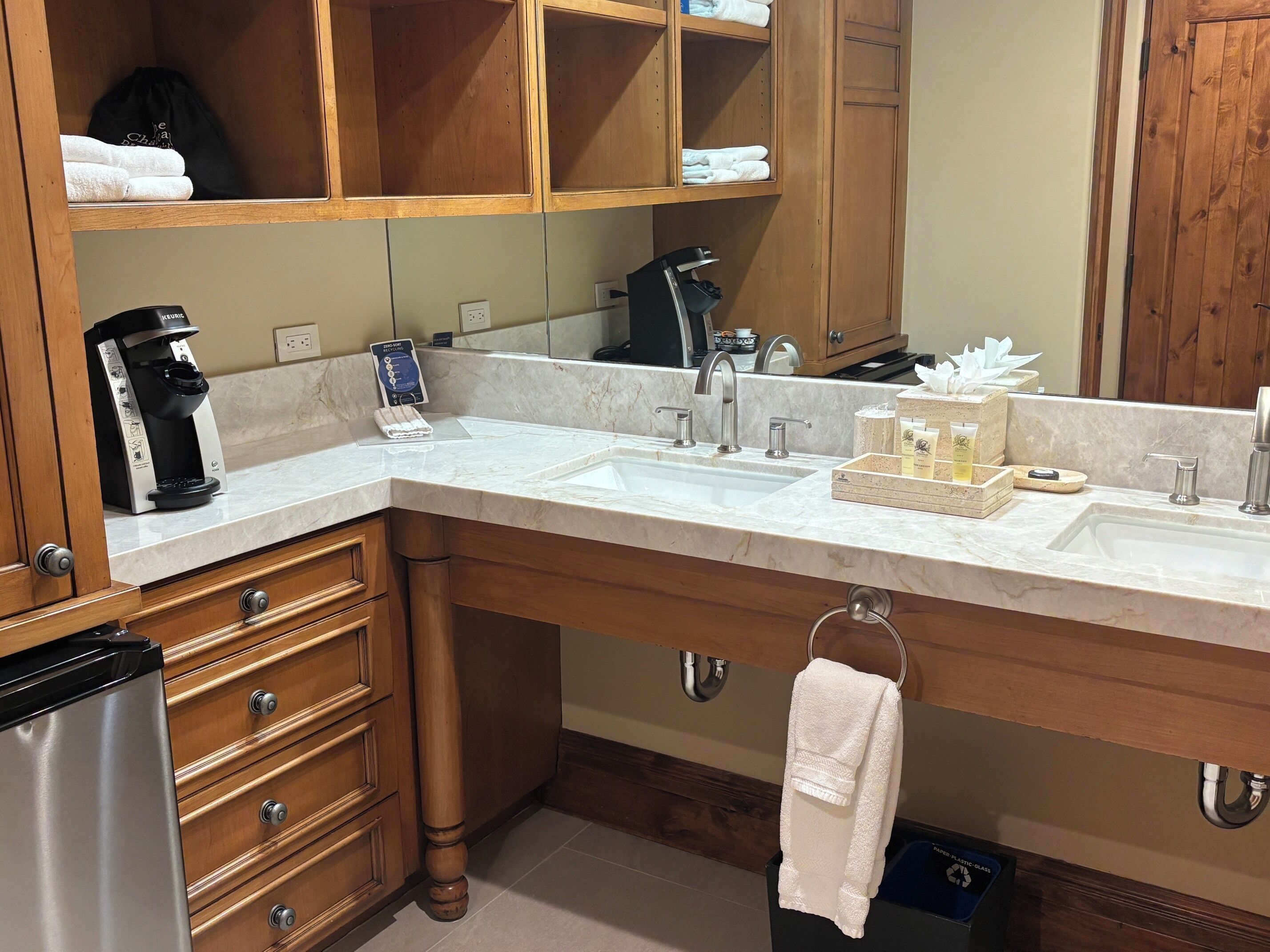 A modern bathroom with a marble countertop, dual sinks, a coffee machine, and a towel rack.