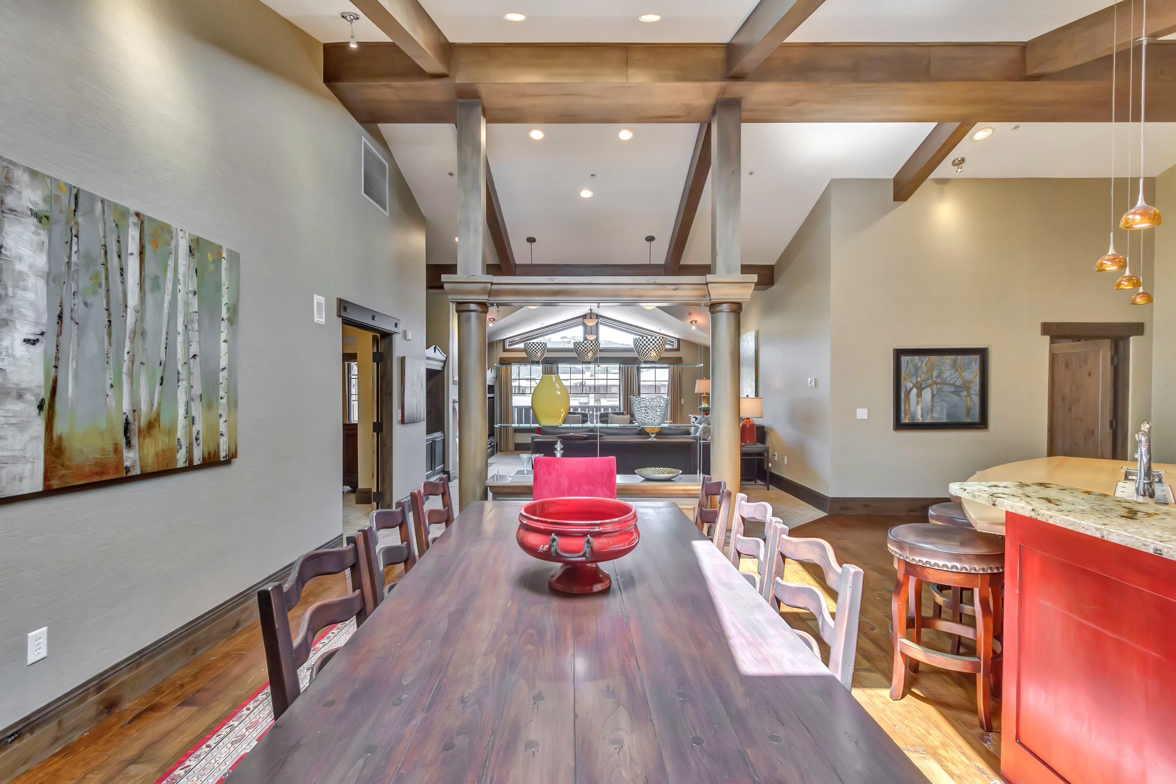 A spacious dining area with a long wooden table, red centerpiece, and modern lighting.