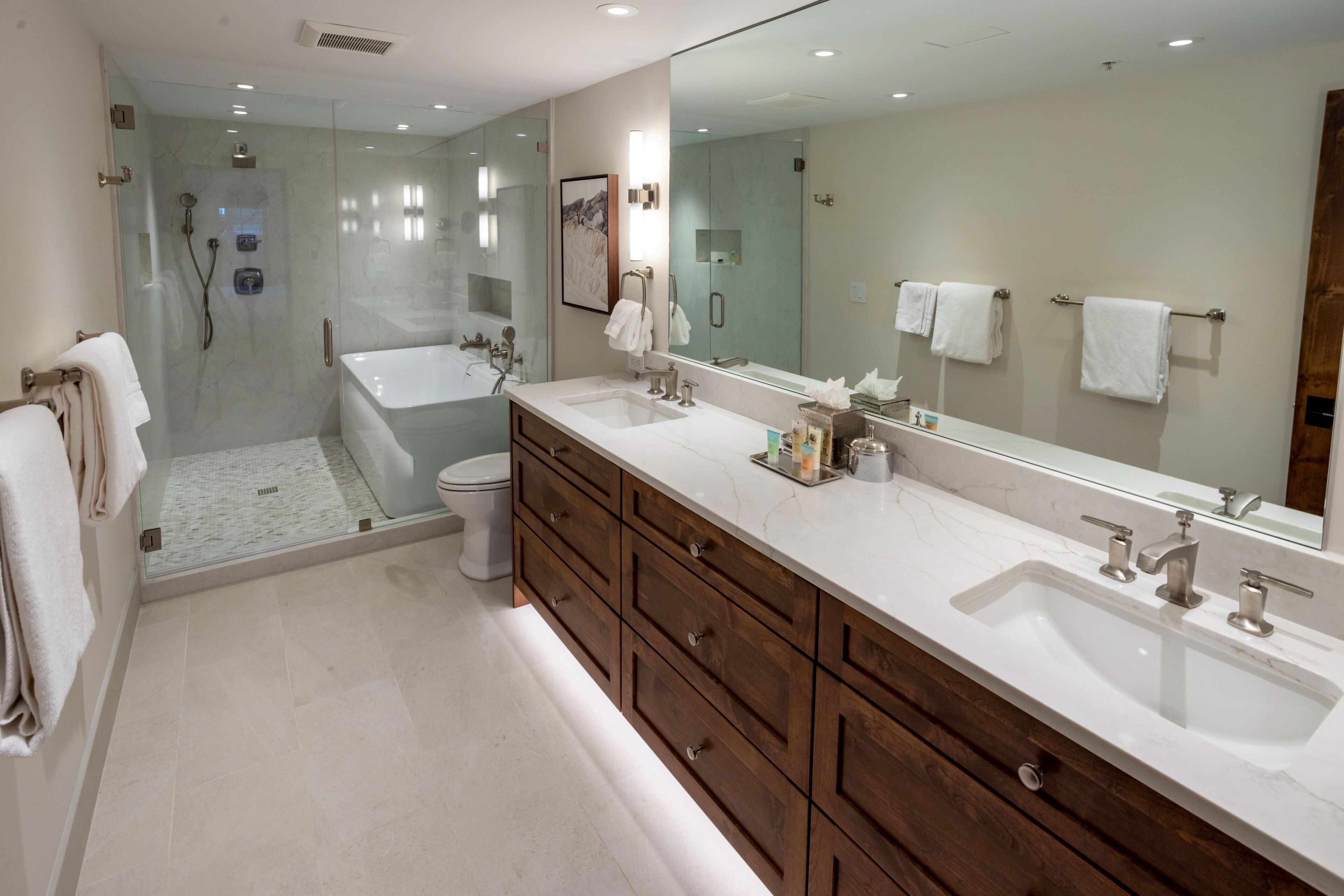 Un baño moderno con ducha envuelta en vidrio, una bañera, un espejo grande y un tocador de madera con lavamanos.