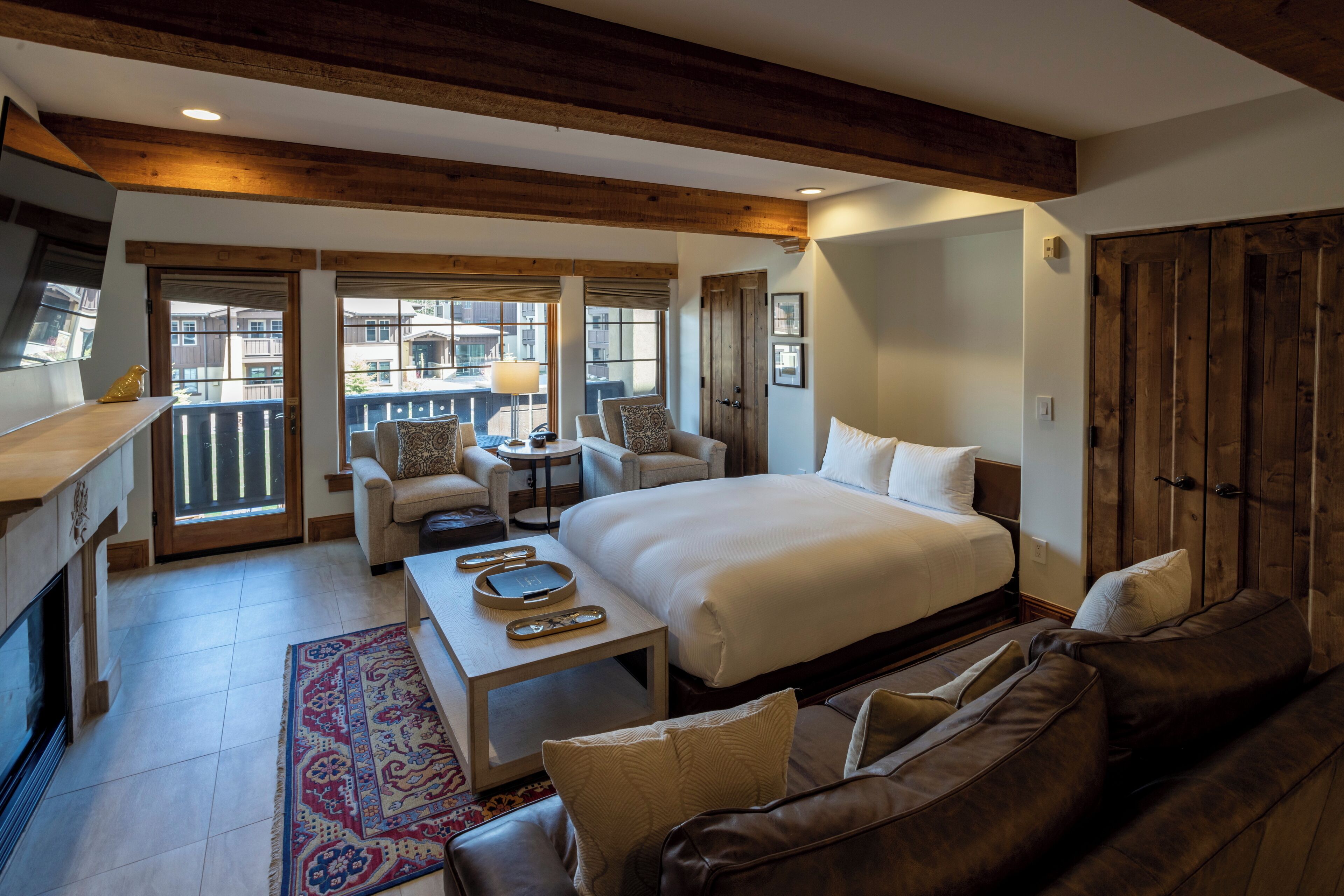 A spacious room with a large bed, a sofa, a small table, and a balcony with a view of the city.