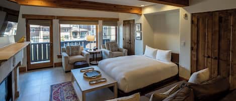 A spacious room with a large bed, a sofa, a small table, and a balcony with a view of the city.