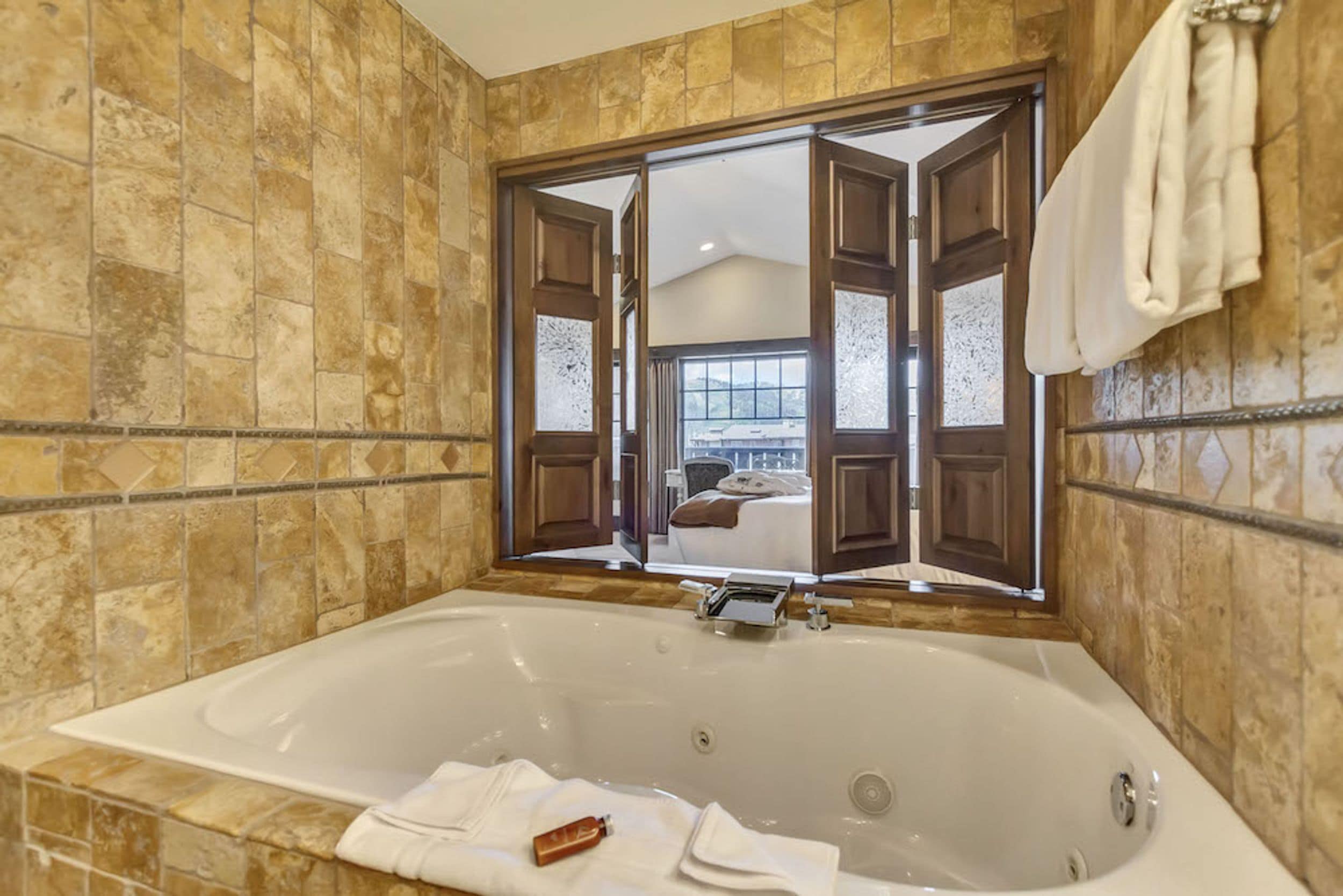 Un baño con una bañera grande, un espejo y una ventana con contraventanas de madera.