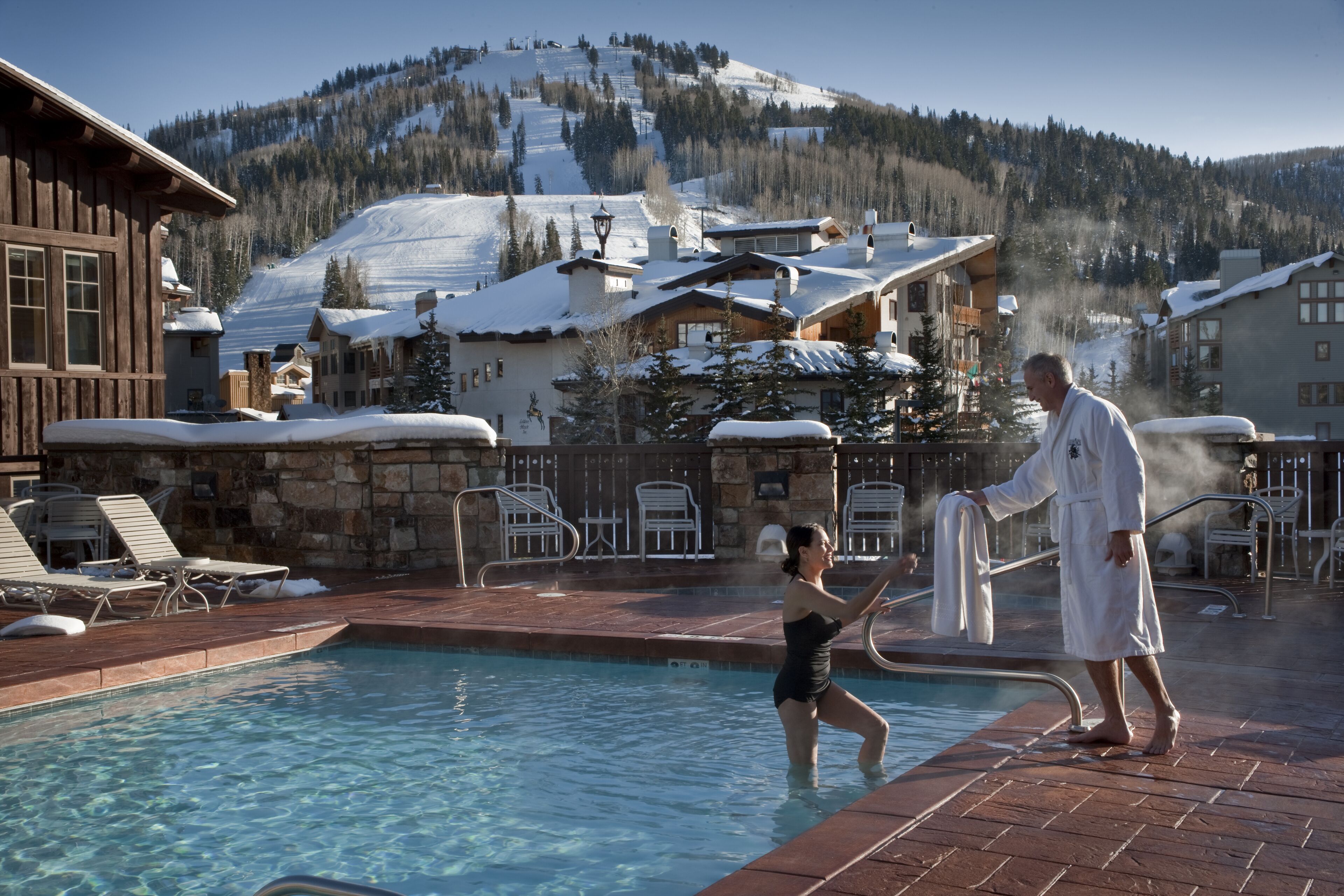 A pool area with clear water, lounge chairs, and a view of snow-covered mountains.