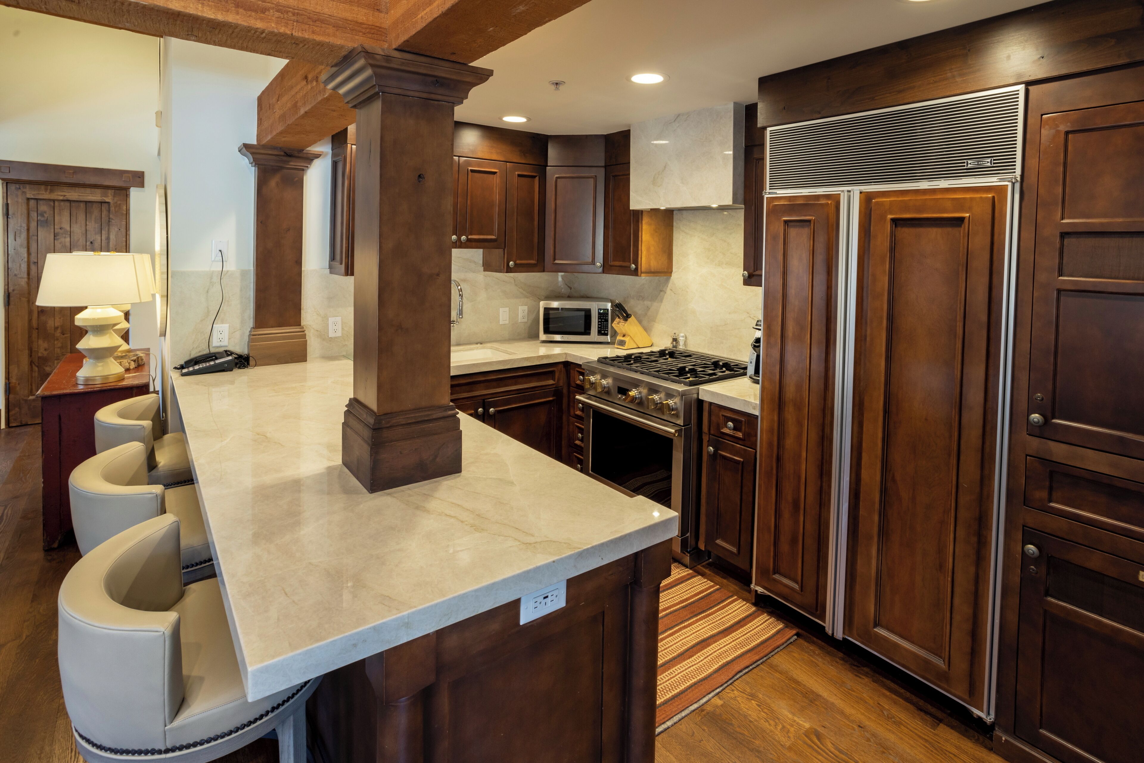 A kitchen with dark wooden cabinets, a marble countertop, a built-in microwave, a stove, and a large refrigerator.