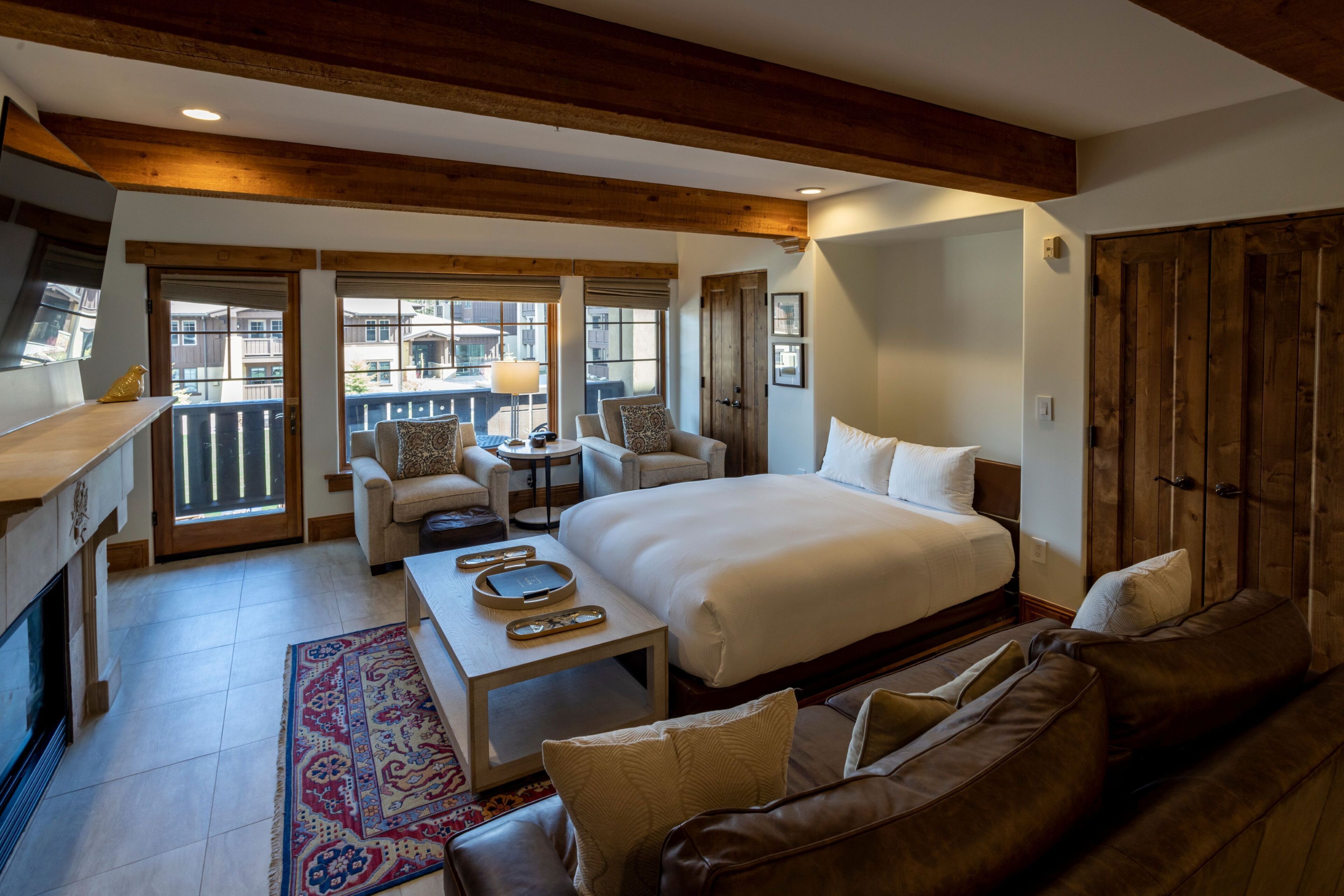 A hotel room with a large bed, a sofa, a small table, and a balcony with a view.