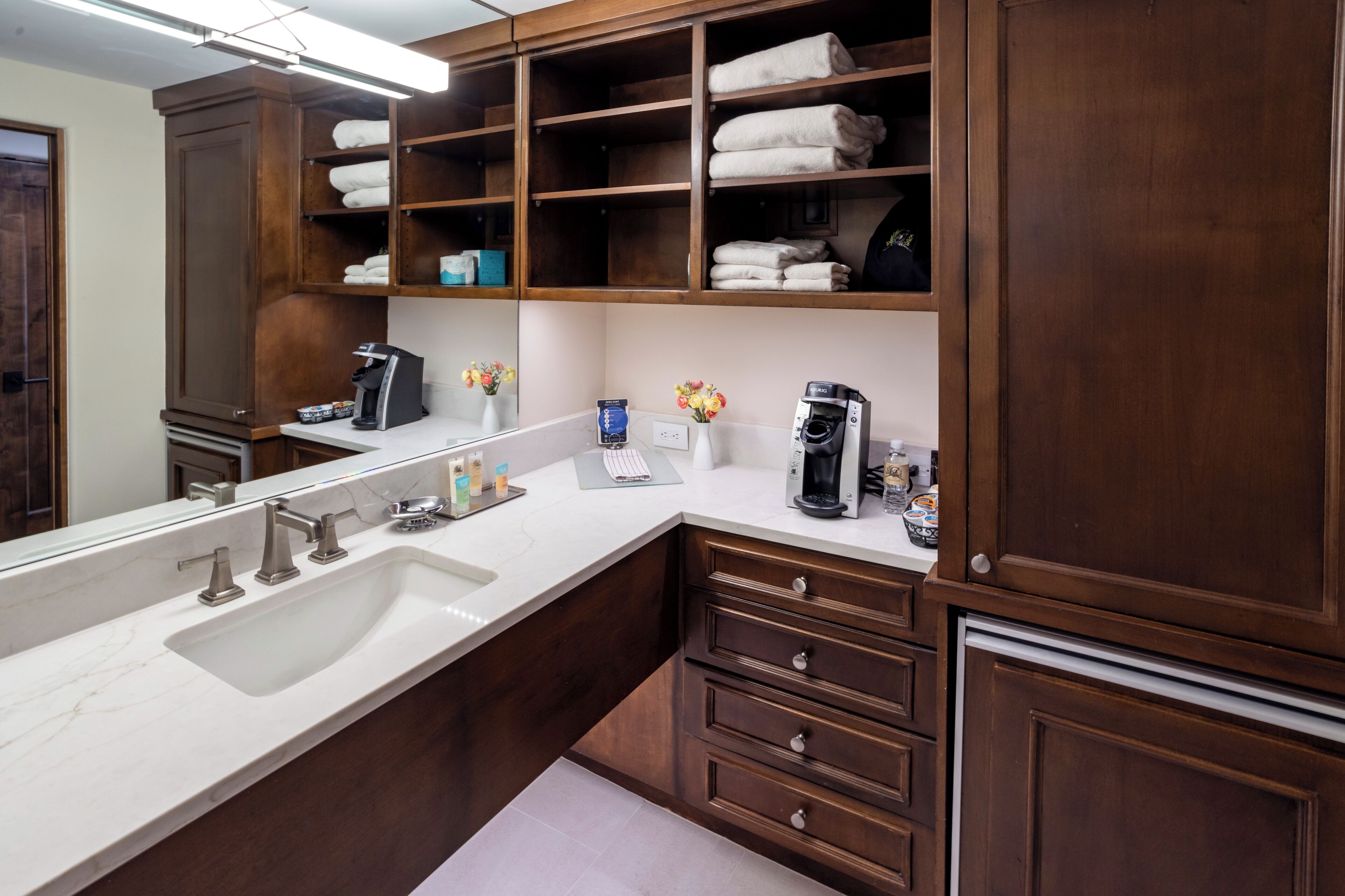 A modern bathroom with a large sink, wooden cabinets, and a coffee maker.