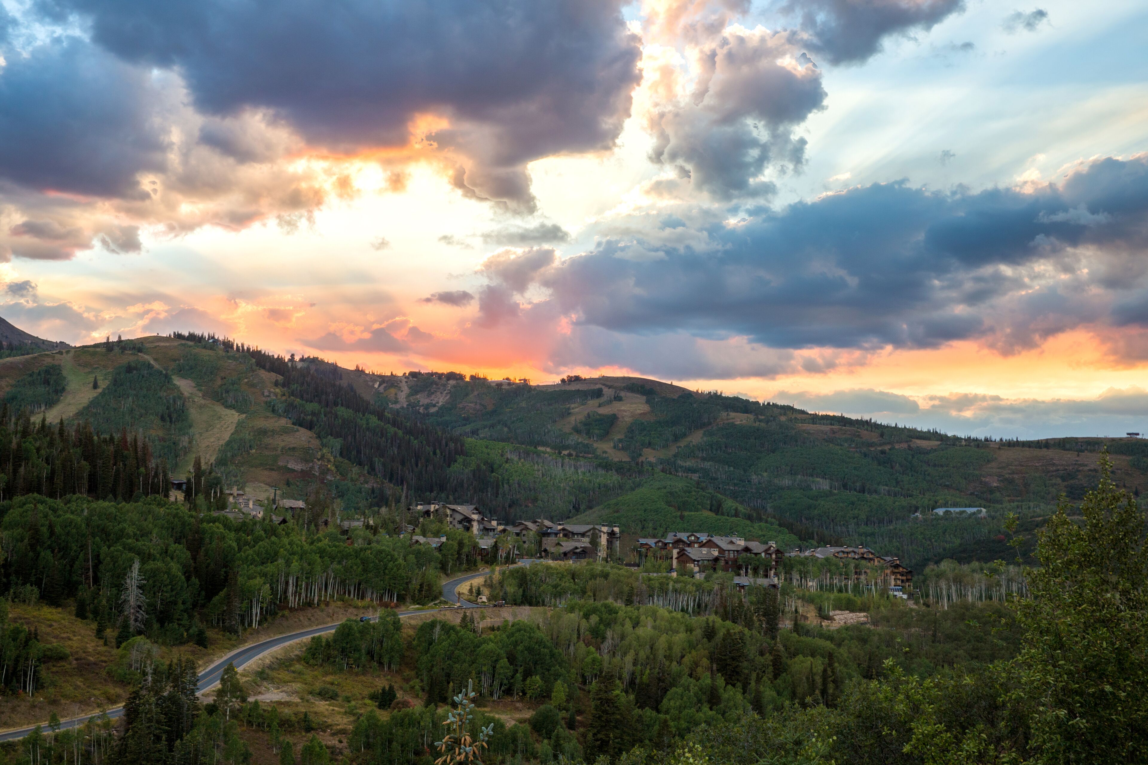 A mountainous landscape with a village nestled among the hills, featuring a winding road and dense forest.