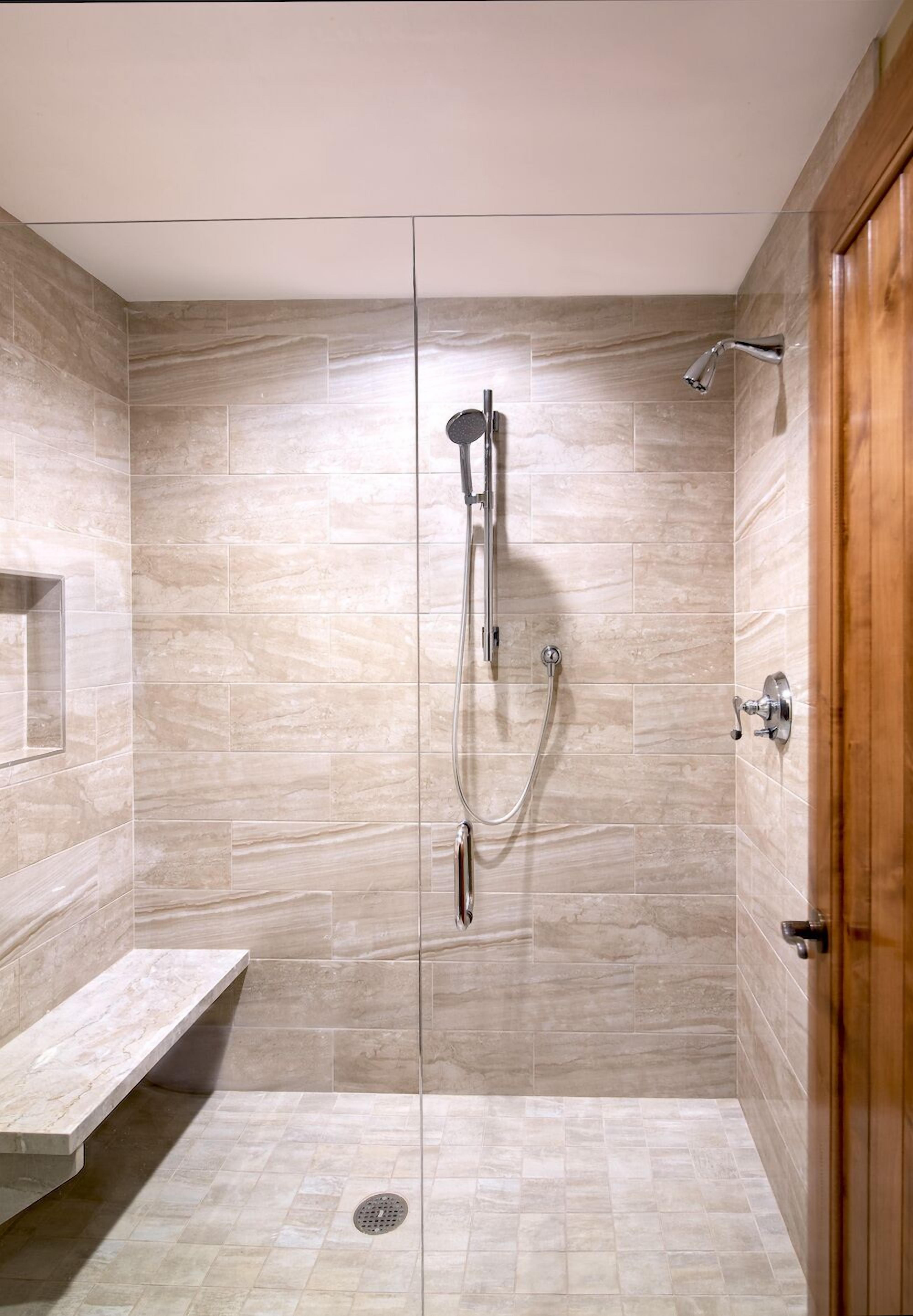 A walk-in shower with a glass door, a bench, and a showerhead.