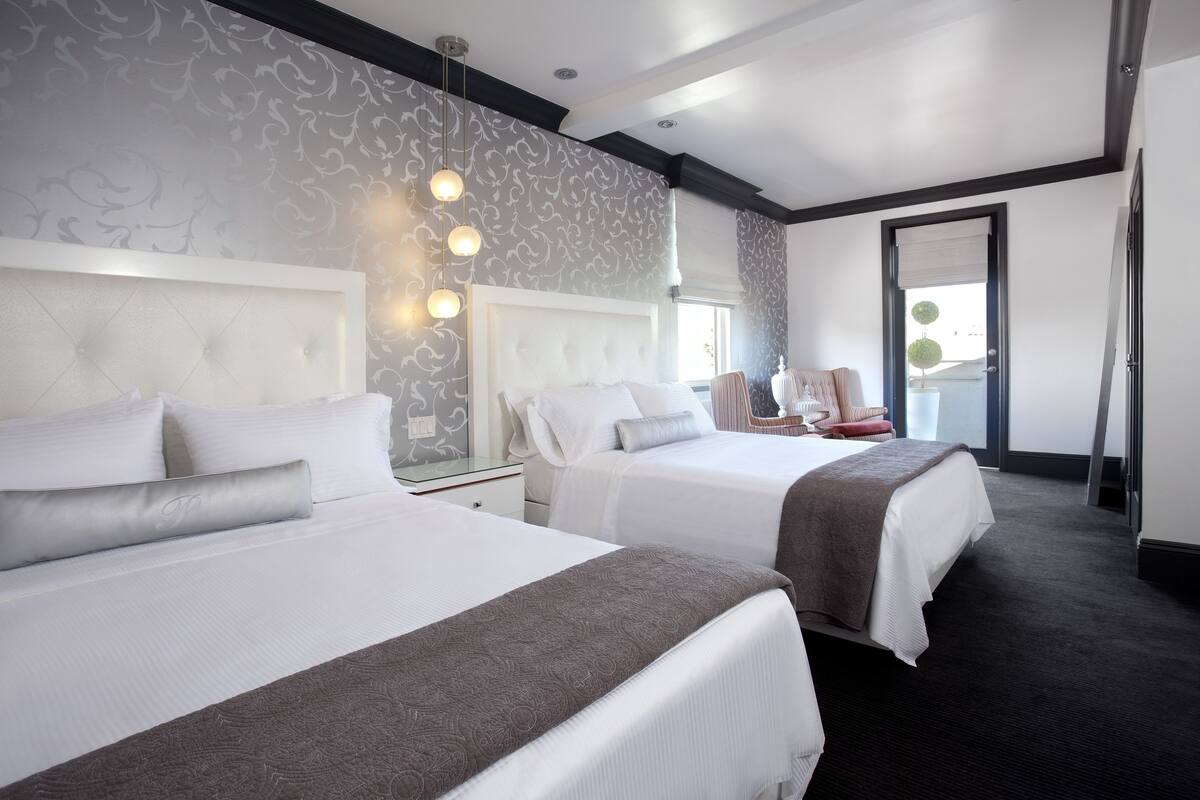Quarto de hotel com duas camas, uma janela grande e uma porta que dá para uma varanda.