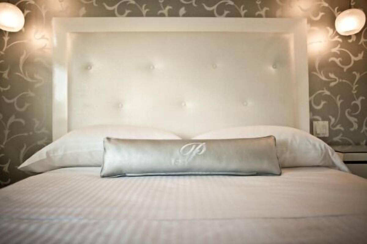 Quarto de hotel com uma cama grande, cabeceira estofada e duas luminárias fixadas na parede.