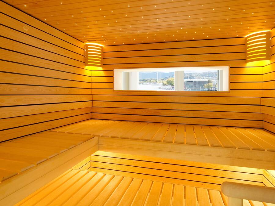 A sauna room with wooden slats on the walls and ceiling, a window with a view, and a bench.