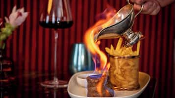 A dish of fries with a small bowl of sauce, a glass of red wine, and a lit candle on a table.