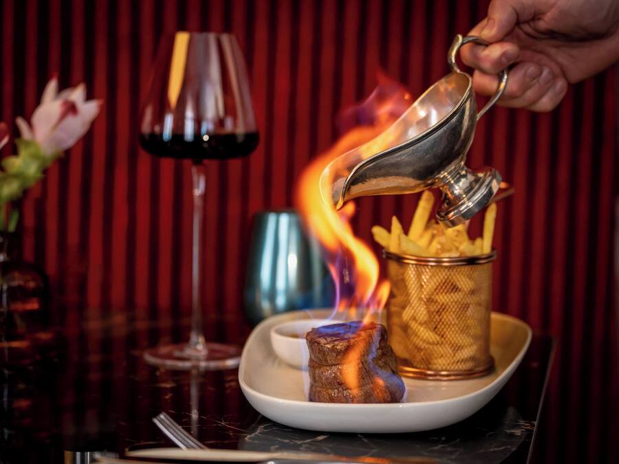 A dish of fries with a small bowl of sauce, a glass of red wine, and a lit candle on a table.