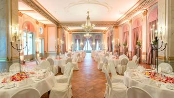 Ein Festsaal mit Reihen runder Tische, festlich für eine Veranstaltung gedeckt, mit weißen Tischdecken und floralen Mittelstücken.
