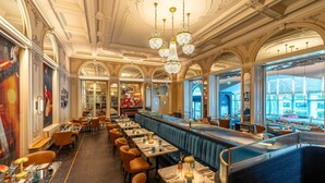 A restaurant with high ceilings, chandeliers, and a long counter with booths. - Hotel Schweizerhof Luzern (Lucerne)