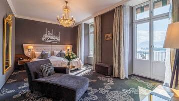 Ein Hotelzimmer mit Bett, einer Couch, einem Chandelier, einem großen Fenster mit Vorhängen und einer Wanddekoration im Schiffsdesign.