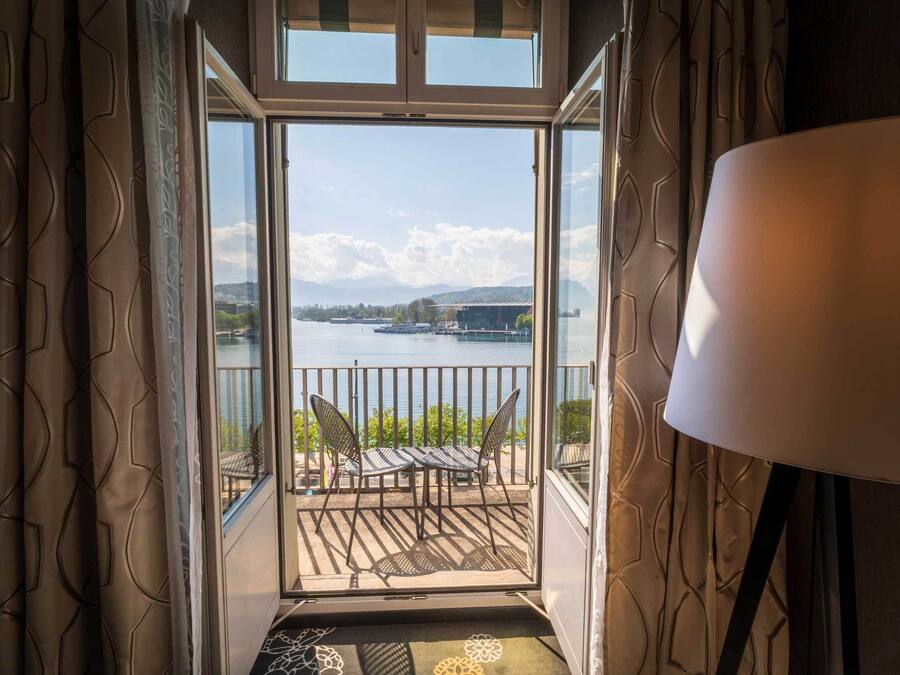 Una habitación con vista a un lago, un balcón con sillas y una lámpara.